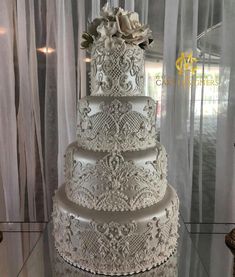 a three tiered wedding cake sitting on top of a table next to sheer curtains