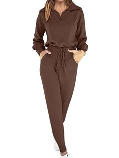 a woman standing in front of a white background wearing a brown hoodie and sweatpants