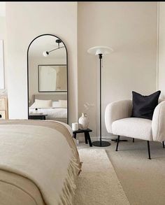 a bedroom with a bed, mirror and two chairs in front of the bed are all white