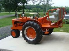 an orange tractor parked on top of a cement slab in front of a park area