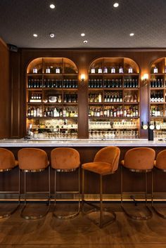 a bar with several chairs and bottles on the wall behind it, along with an array of liquor bottles