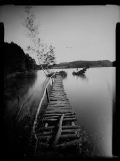 an old photo of a wooden dock in the middle of a body of water with trees on both sides