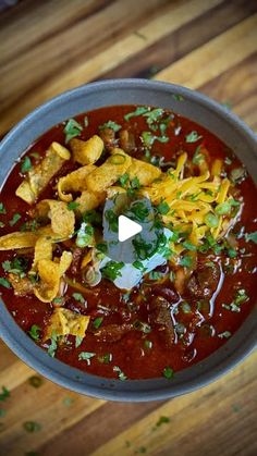 a bowl filled with chili and tortilla chips on top of a wooden table