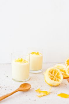 two glasses filled with orange juice next to sliced lemons and a wooden spoon on a white surface