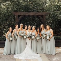 a group of women standing next to each other in front of a gazebo with greenery