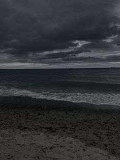 a black and white photo of the ocean with dark clouds above it, as seen from a beach