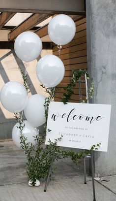 a welcome sign with white balloons and greenery