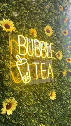 a sign that says bubble tea with sunflowers in the foreground and behind it is a green wall