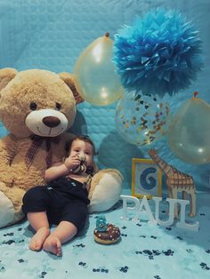 a baby is sitting in front of a teddy bear with balloons and decorations around it