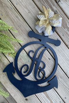 a metal monogrammed ornament with an anchor and bow sits on a wooden surface