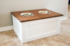 two metal bowls on top of a white dog bowl stand in a room with tile flooring