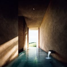 an indoor swimming pool in the middle of a room with sunlight coming through it and water running down the wall