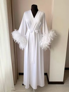 a white robe with feathers on it and a mannequin in the corner behind it