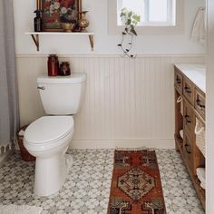 a white toilet sitting in a bathroom next to a sink under a window on top of a rug