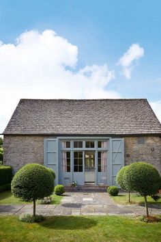 an old stone building with blue shutters and two chairs in the front lawn area