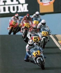 several motorcyclists racing down a race track in front of a large sign