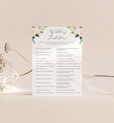 a white wedding program with flowers and greenery on it, sitting next to a flower vase