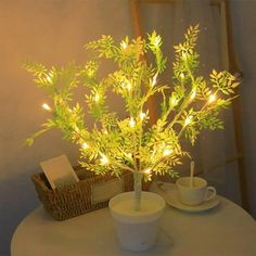 a white table topped with two cups and a tree filled with lights next to a basket