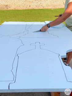 a person cutting out a piece of paper on top of a white table with scissors