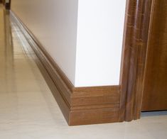 an empty hallway with white walls and wood trimmings on the floor, in front of a door