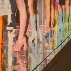 several women's legs in high heeled boots standing on the floor with their reflection