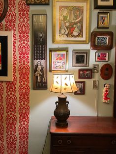 a lamp sitting on top of a wooden table next to a wall covered in pictures