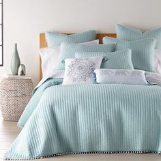 a bed covered in blue and white comforter next to a vase with flowers on it