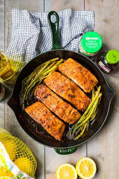 salmon and asparagus in a cast iron skillet with lemons on the side