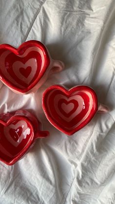 three red heart shaped dishes sitting on top of a white sheet