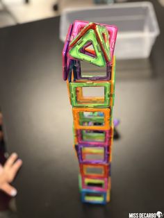 a stack of colorful plastic blocks sitting on top of a black table next to a child's hand