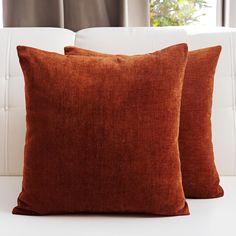 two brown pillows sitting on top of a white couch next to each other in front of a window