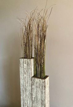 two wooden vases with grass in them on a table next to a white wall