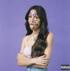 a woman with her arms crossed and painted in sugar skulls on her face, standing against a purple background