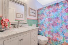 a bathroom with a colorful shower curtain next to a white toilet and sink in front of a mirror