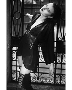 black and white photo of woman in short dress with boots on her feet, leaning against iron gate