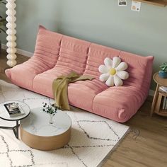 a living room with a pink couch, coffee table and potted plant on the floor