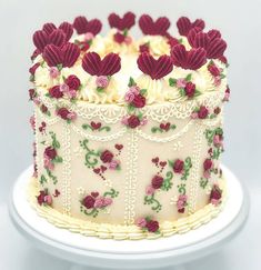 a white cake with red and pink flowers on it is sitting on a platter