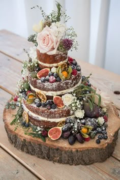 a three tiered cake with fresh fruit and flowers on top is sitting on a wooden table