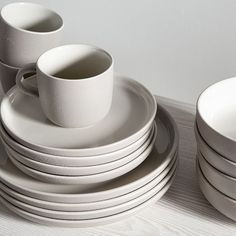 a stack of white plates and cups sitting on top of a wooden table next to each other