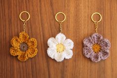 three crocheted flower keychains hanging on a wooden surface with gold rings