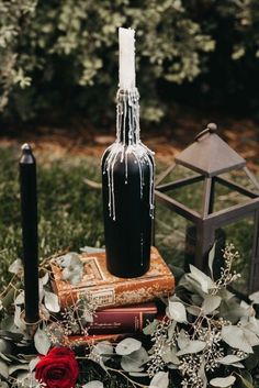 a black bottle with icing on it sitting next to some books and candles in the grass