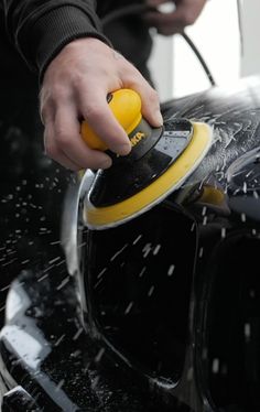 a person polishing a car with a yellow and black orbital sander on it