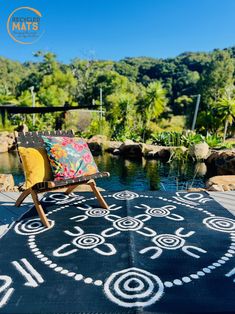 a chair sitting on top of a black rug next to a lake and forest in the background