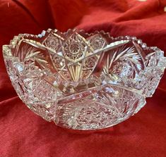 a clear glass bowl sitting on top of a red cloth covered tablecloth with an ornate design