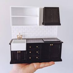 a hand holding a miniature model of a kitchen with sink, cabinets and cupboards