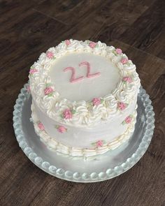 a white cake with pink frosting and flowers on it sitting on top of a wooden table