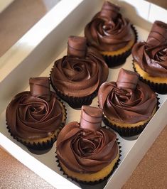 six cupcakes with chocolate frosting in a white box on a brown table