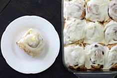 a white plate topped with food next to a pan filled with cinnamon rolls