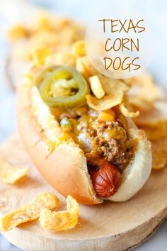 a hot dog with toppings and chips on a wooden board that says texas corn dogs