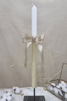 a white candle is sitting on a stand with a ribbon around it and cotton balls in the background